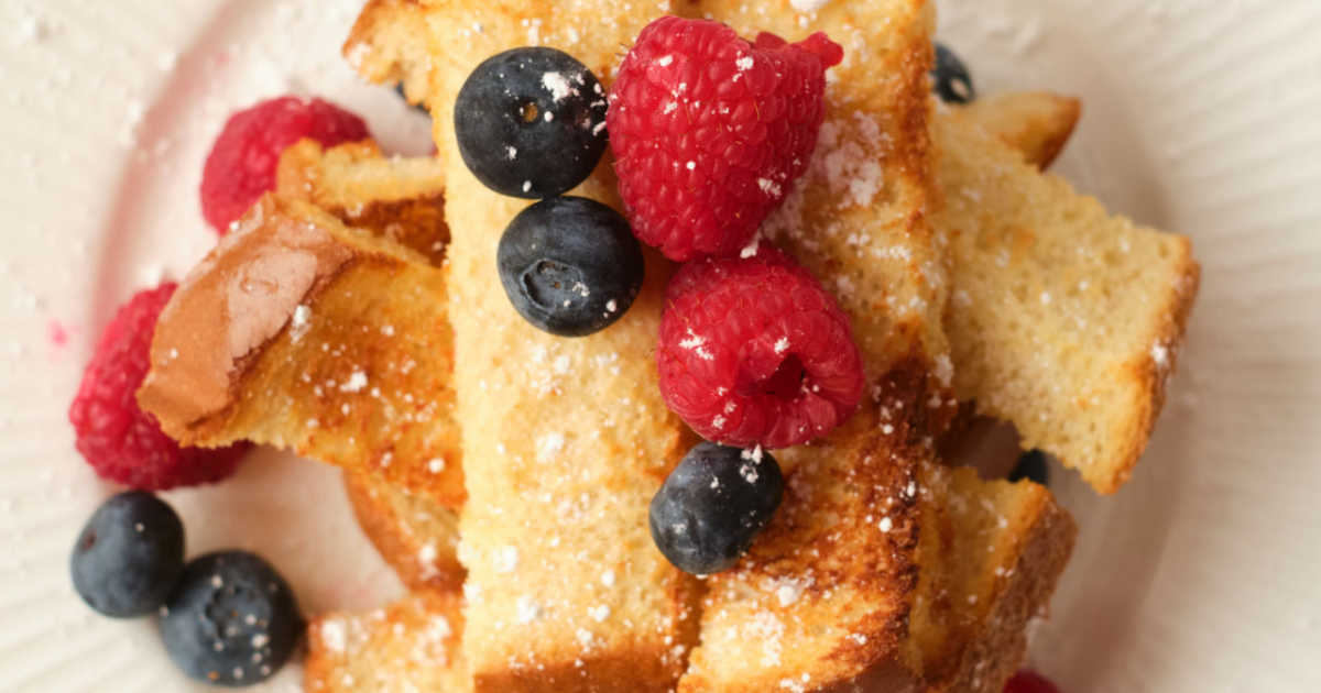 french toast sticks sprinkled with powdered sugar and topped with fresh berries.