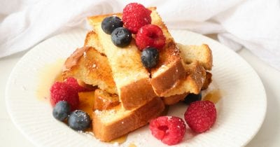 Air fryer egg-free french toast sticks topped with fresh berries served on white plate.