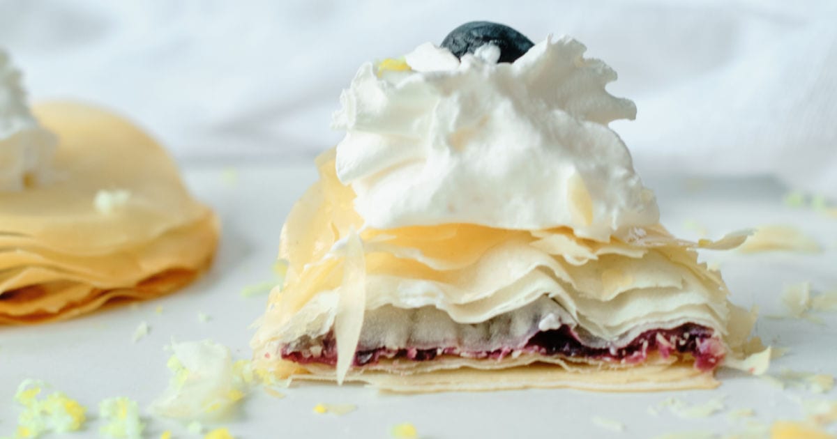 side view of blueberry filo dough pastry topped with whipped cream.