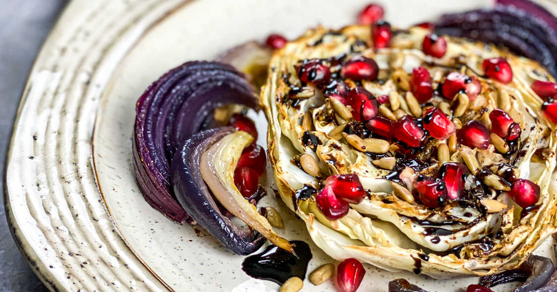 stoneware plate with cabbage steak topped with pomegranate arils and sunflower seeds.