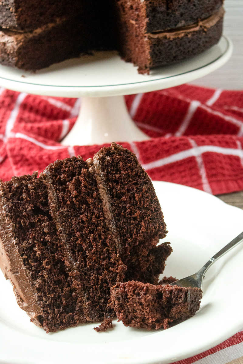 slice of chocolate layer cake on a plate with whole cake in background.